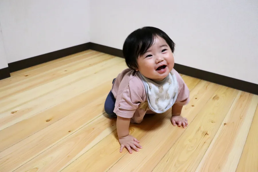 桧の無垢フローリングの上で笑顔でハイハイする作り手の娘